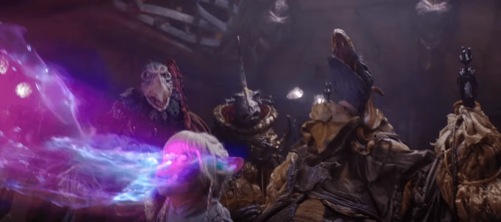 Skeksis stand behind Gelfling as pulsing energy is drawn out of her