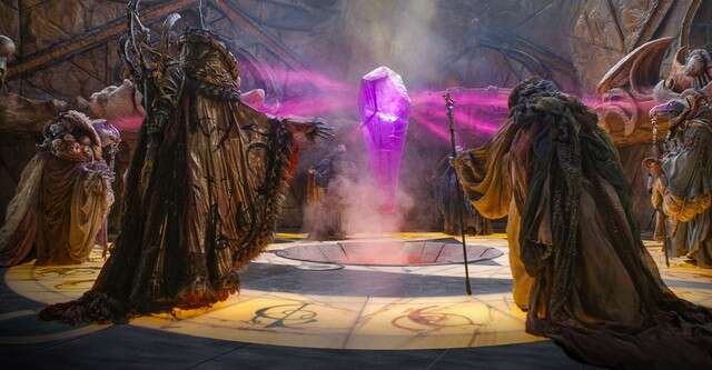 Robed Skeksis surround and absorb energy from a purple crystal